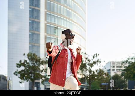 Happy excited young African man in headphones dancing on city street. Stock Photo