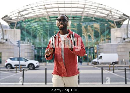 Happy Black hipster man in headphones listening music dancing on city street. Stock Photo
