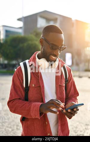 Young happy African man standing on city street using mobile phone. Vertical Stock Photo