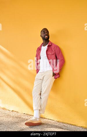 Smiling cool gen z Black hipster guy looking away standing at yellow wall. Stock Photo