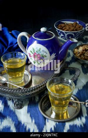 Two glasses of green tea with a Russian Gardner porcelain teapot with royal blue glaze, on an antique silver tray, with blue and white ikat material Stock Photo