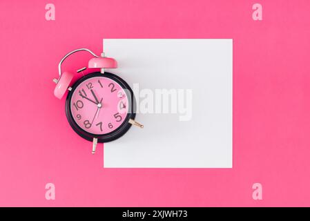 Pink and black retro alarm clock on pink background with white paper card note copy space. Minimal time concept. Flat lay. Stock Photo