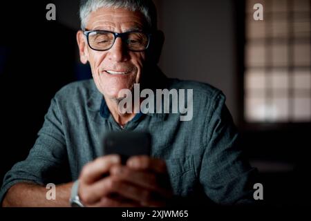 Senior man, night and phone in office for texting with communication, networking and reading email. Elderly employee, mobile connection and typing Stock Photo