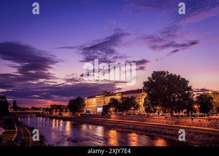 A view of the Nisava River in Nis, Serbia, as the sun sets and the city lights illuminate the buildings along the banks. Stock Photo