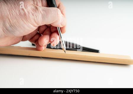 carpenter marking a wooden plank with a mechanical pencil used for woodworking isolated on a white background Stock Photo