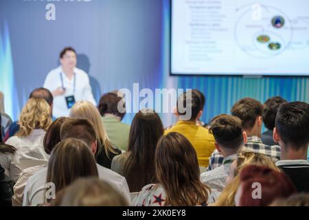 Diverse audience is attentively listening to a business presentation during a professional conference. The speaker is visible in the background giving the presentation. Stock Photo