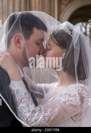 Wedding portrait of the bride and groom. Happy bride and groom gently hug each other under the veil, gently look into each other's eyes. Love, new fam Stock Photo