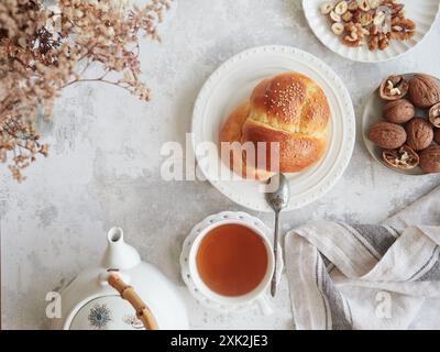 From above of serene autumn tea setting featuring a freshly baked challah bread, a steaming cup of tea, and a selection of walnuts and hazelnuts Stock Photo