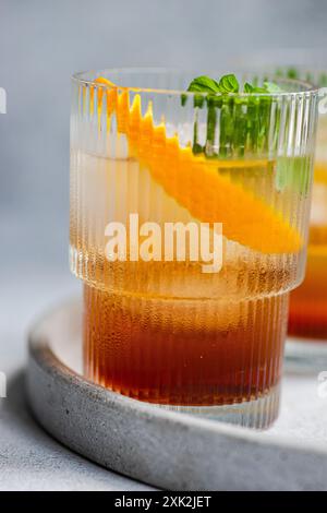 A vibrant summer cocktail featuring cherry liqueur and tonic, served with ice, a fresh orange slice, and mint leaves in a stylish glass on a concrete Stock Photo