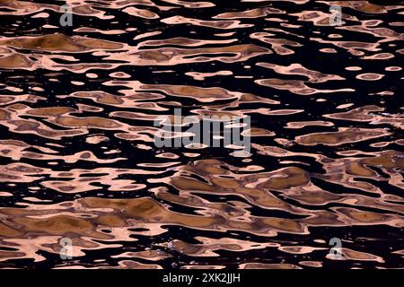A high-contrast abstract image of the sea surface reflecting sunlight, featuring swirling patterns and dark backgrounds, emphasizing the interplay of Stock Photo