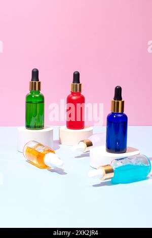 A vibrant display of multicolored dropper bottles placed on various podiums against a pink background, depicting a modern cosmetic setup Stock Photo