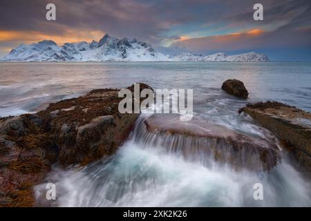 Majestic view of the Lofoten Islands under a fiery sunrise with snow-covered peaks and turbulent ocean waters in winter Stock Photo