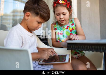 Six year old brother and sister playing on tablet while sitting on balcony. Screen time control concept for kids. Stock Photo