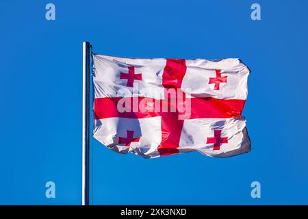 Large Georgian flag on a flagpole waving against the blue sky Stock Photo