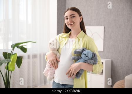 Expecting twins. Pregnant woman holding two toys at home Stock Photo