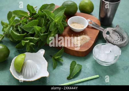 Wooden cutting board, juicer and ingredients for mojito on green background, closeup Stock Photo