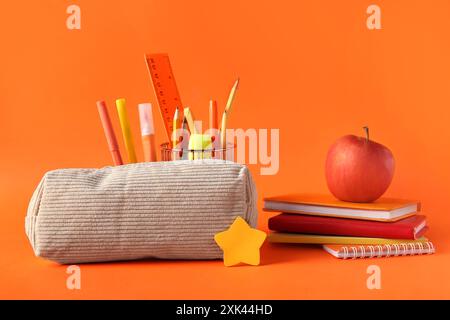 Beige pencil case with different stationery and apple on orange background Stock Photo