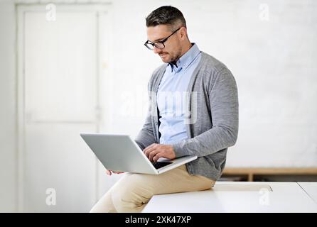 Laptop, office and man on desk working for it support in startup company for project. Reading, pride and male software engineer with computer for Stock Photo