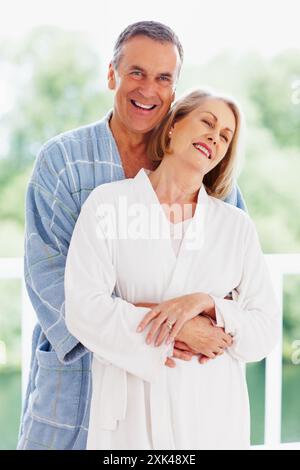 Portrait, support and balcony with mature couple, love and hug in living room of house together. Smile, face and trust with happy, senior man and Stock Photo