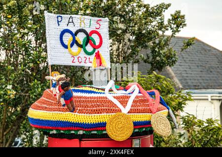 Colourful knitted post box topper celebrating the Paris 2024 Olympics with crocheted medals, athletes, flame and Olympic Rings, Weymouth, Dorset Stock Photo