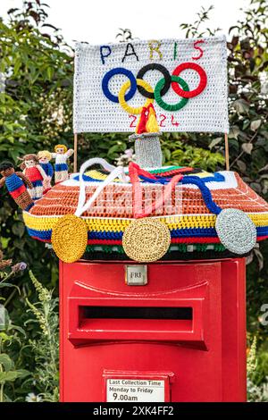 Colourful knitted post box topper celebrating the Paris 2024 Olympics with crocheted medals, athletes, flame and Olympic Rings, Weymouth, Dorset Stock Photo