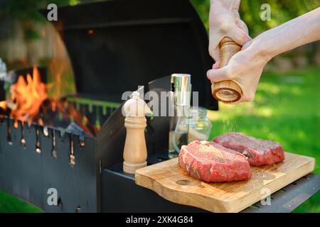 A close-up view of hands using a wooden hand mill to season beef steak with pepper Stock Photo