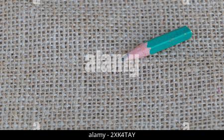 Minimalistic background with pencil on burlap fabric, copy space concept. Top view photo of green crayon on rough cloth texture. Stock Photo