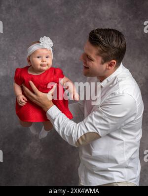 Happy new dad plays with cute baby, lifts, throws adorable daughter in the air, holds baby in arms with love, smiles, laughs, enjoys fatherhood, paren Stock Photo