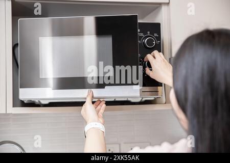 people using the microwave oven, women adjust time to reheat warm food in microwave. Stock Photo