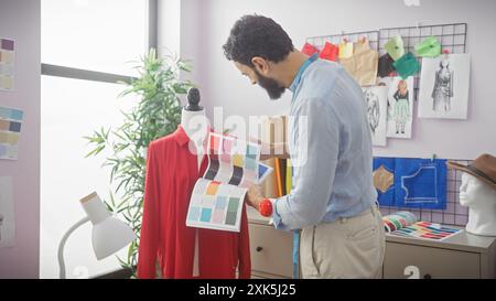 A bearded designer analyzing color palettes in a bright tailoring studio with mannequins, fabric, and sketches. Stock Photo