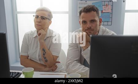 Woman and man sit thoughtfully in an office environment, suggesting business colleagues or partners focused on a project, with a modern workspace back Stock Photo