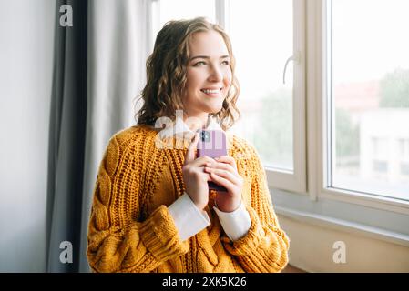 Cheerful Woman Using Smartphone, A close-up shot of a happy, curly-haired woman smiling while browsing the internet on her smartphone. ideal for Stock Photo