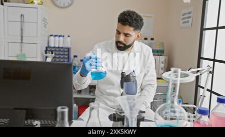 A young man examines a flask in a laboratory setting, showcasing his beard and a professional, focused demeanor. Stock Photo