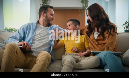 Man woman parents freelancer working remote at home on couch using laptop kid boy child distract mom and dad from work loving caring mother father Stock Photo