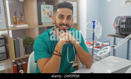A handsome young hispanic man wearing a green uniform and a stethoscope smiles confidently in a veterinary clinic office. Stock Photo