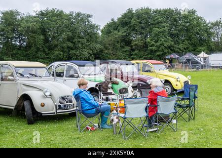 Ballymena, Northern Ireland - July 20th, 2024: ladies seated in front of a row of classic French Citroen 2CV cars. Concept vintage, chic, retro, motor Stock Photo