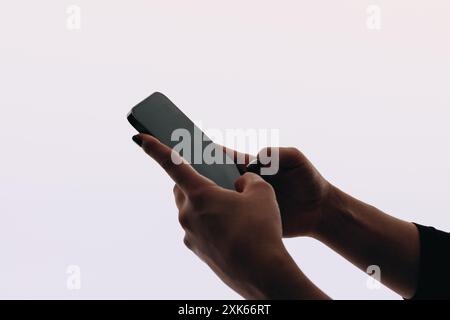 Female hands holding a smartphone in a studio, typing and scrolling a social media app. Woman connecting to the virtual world by engaging in text mess Stock Photo