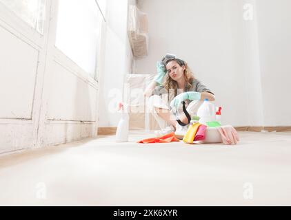 Tired and Disgusted worried Woman by cleaning mold on the home window wall holds a protective respiratory mask. Using household cleaning products to r Stock Photo