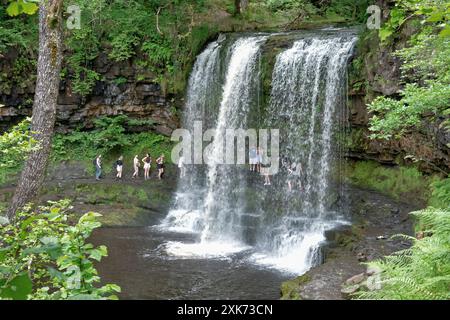 Walkers and visitors to the Brecon Beacons National Park in Wales queuing to walk behind Sgwd Yr Eira A spectacular waterfall on the Afon Hepste river Stock Photo