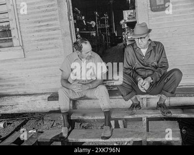Macedonia, Arkansas, United States – June 27, 2024: Horizontal shot of two old friends sitting outside on the steps of an old country store. Stock Photo