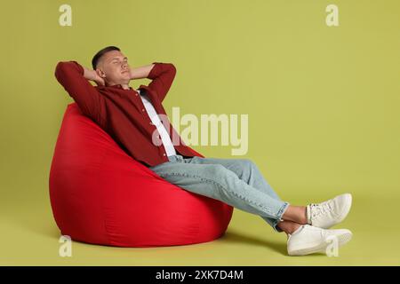 Handsome man resting on red bean bag chair against green background Stock Photo