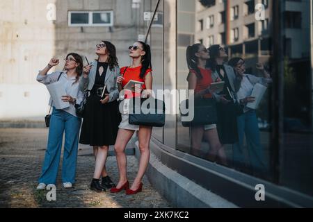 Three businesswomen collaborating outdoors, analyzing blueprints and planning project Stock Photo