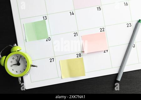 Timetable. Planner with sticky notes, pen and alarm clock on black wooden table, top view Stock Photo