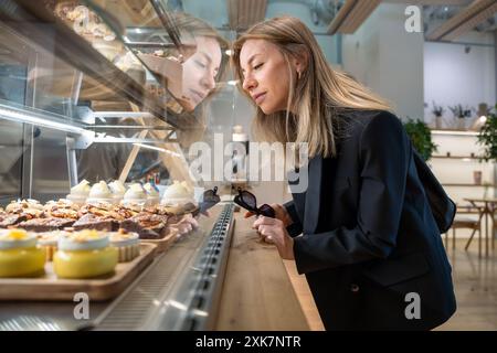 Smiling modern woman chooses cream and chocolate pastries at confectionary window. Sugar free sweets Stock Photo