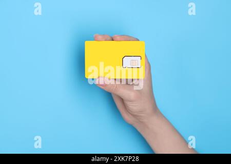 Woman holding SIM card on light blue background, closeup Stock Photo