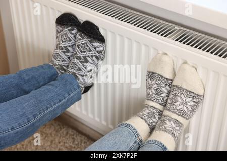 Couple warming feet near heating radiator at home, closeup Stock Photo