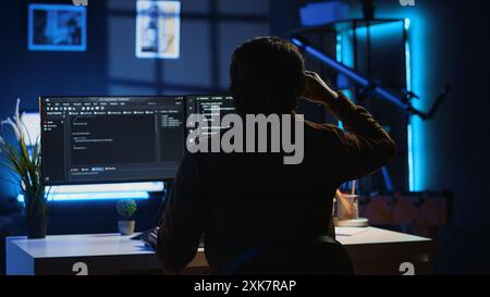 Man doing IT support job from apartment personal office drinking cup of coffee while coding. Software developer enjoying hot beverage and writing lines of code on computer, camera A Stock Photo