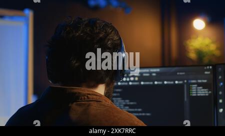 Technician putting headphones on while using coding to fortify firewalls, teleworking for IT company. Computer scientist listening music and upgrading binary code scripts in home office, camera A Stock Photo