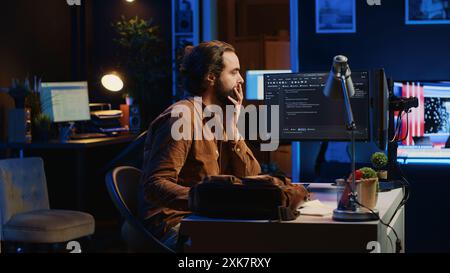 Freelancing system administrator arriving in personal office at home, resuming work on coding. IT expert starting job in apartment, writing lines of code on computer, camera A Stock Photo