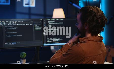 Happy self employed developer in home office doing coding on computer at desk. Joyful IT specialist doing contracted job from apartment, writing lines of code at workstation, camera A Stock Photo